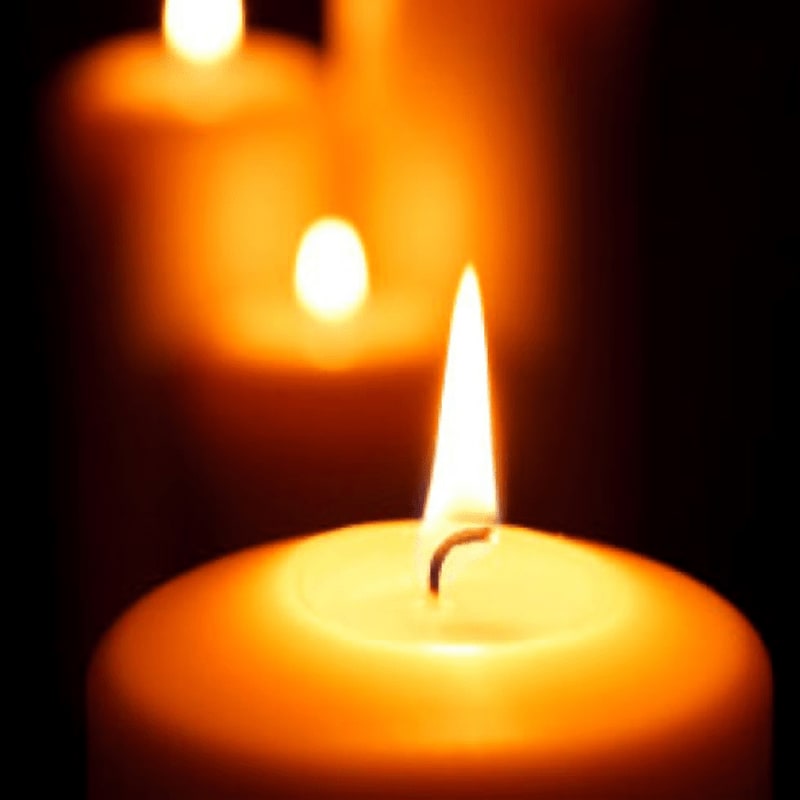 A close-up of a lit candle in the foreground is set against a blurred background of two other glowing candles.