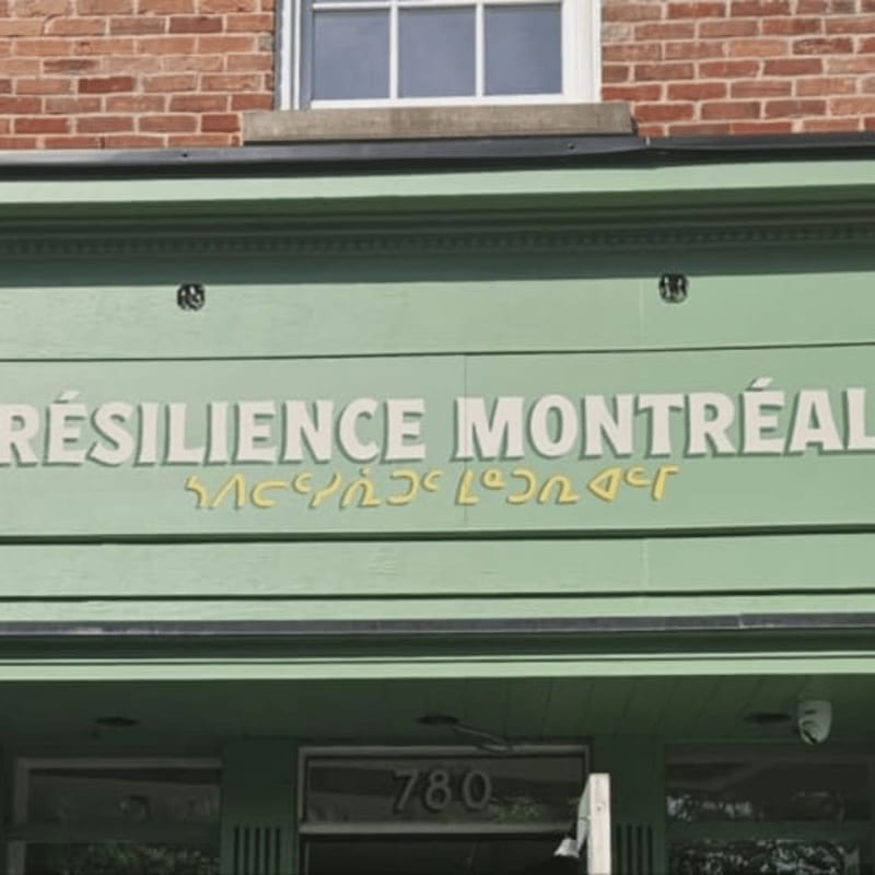 A pale green awning with "RÉSILIENCE MONTRÉAL" in white letters is mounted on a brick building with windows above.