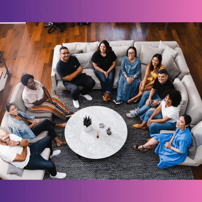 A diverse group of people are gathered in a circle around a coffee table in a modern living room.