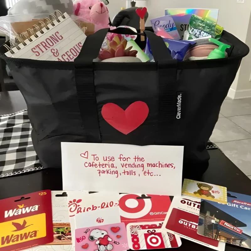 A black tote bag filled with gifts sits on a table in front of a collection of gift cards, with a note explaining their purpose.