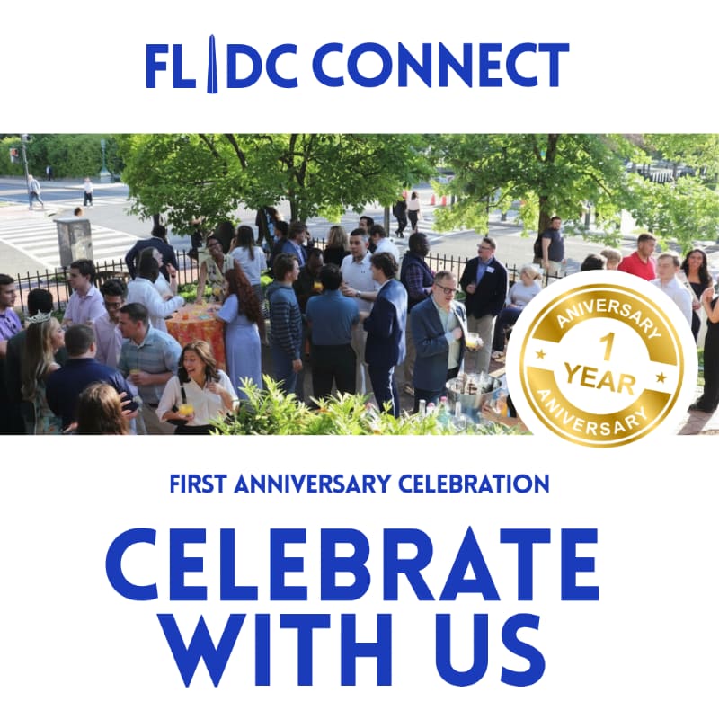 A group of people mingle at an outdoor event with trees and buildings in the background, while a "1 Year Anniversary" seal is prominently displayed.