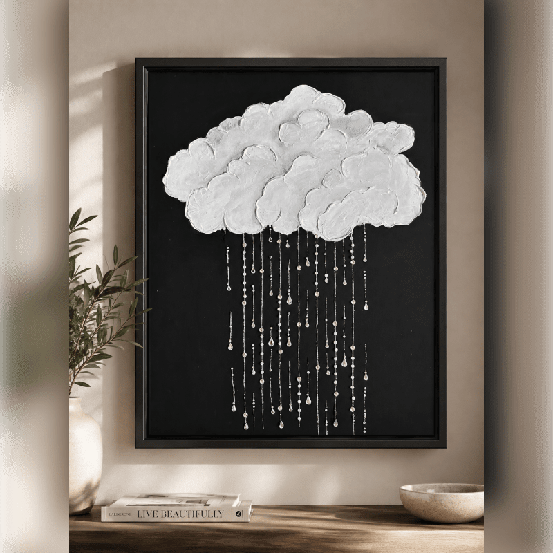 A textured white cloud with dangling raindrops is set against a stark black background, with a vase of greenery and a book visible in the foreground.