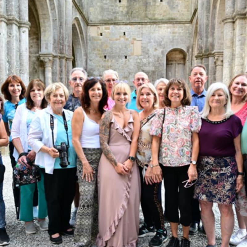 A group of smiling people pose in front of a weathered stone building with arched windows.