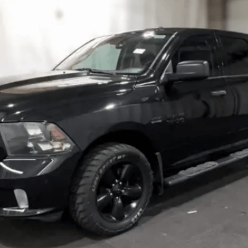 A shiny black pickup truck with black rims sits in a dimly lit garage.