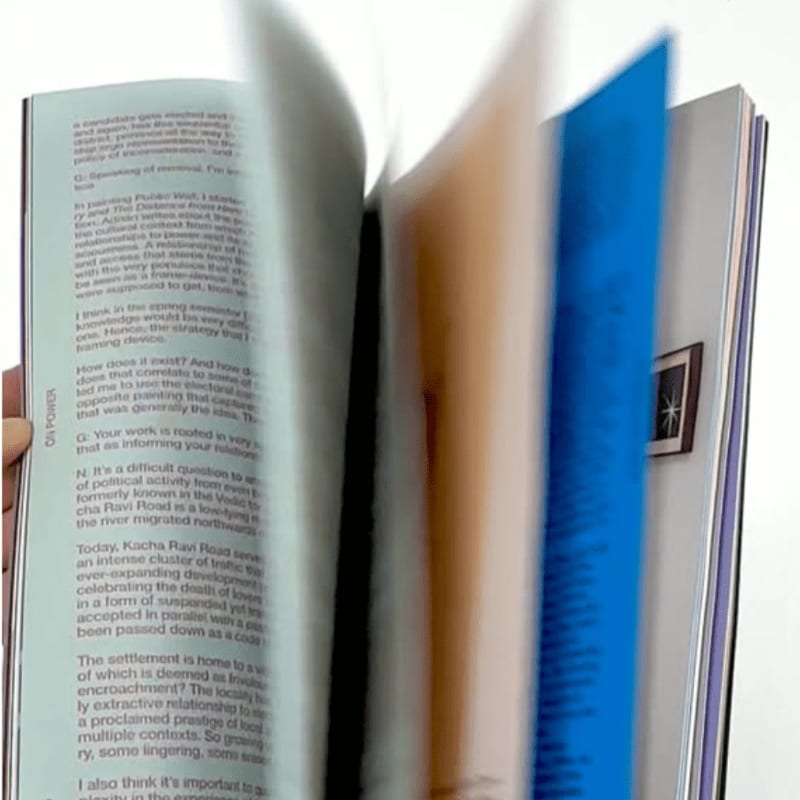 A hand holds open a book with blurred pages, revealing text and a blue page in the background.