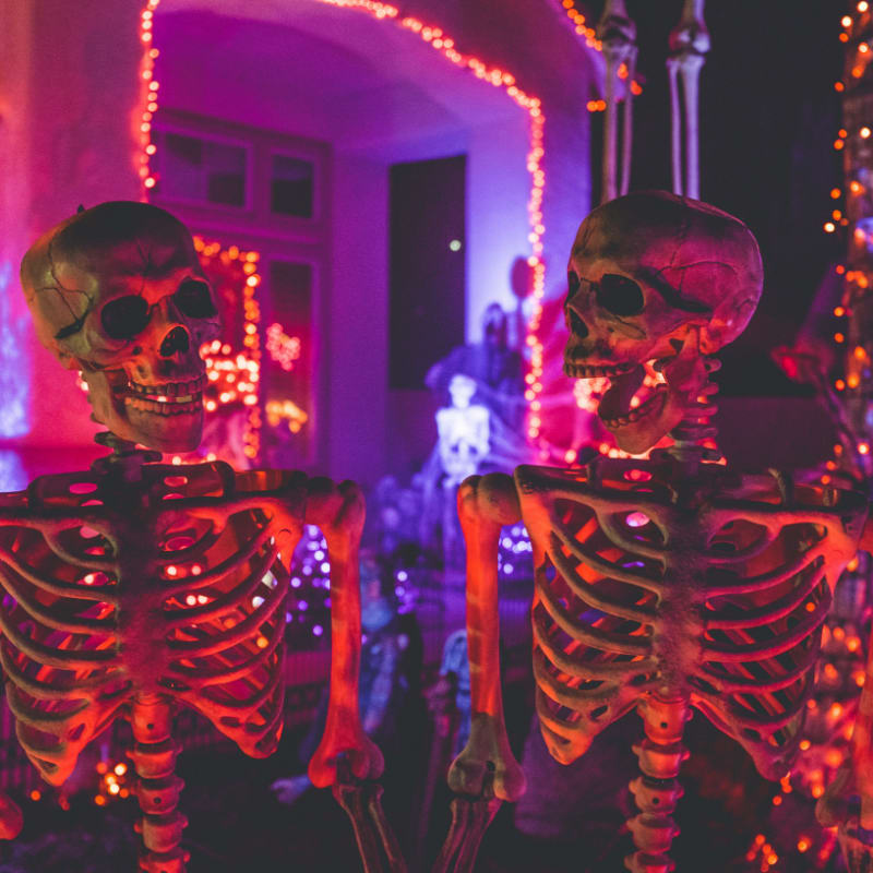 two skeleton near white concrete building with string lights at daytime