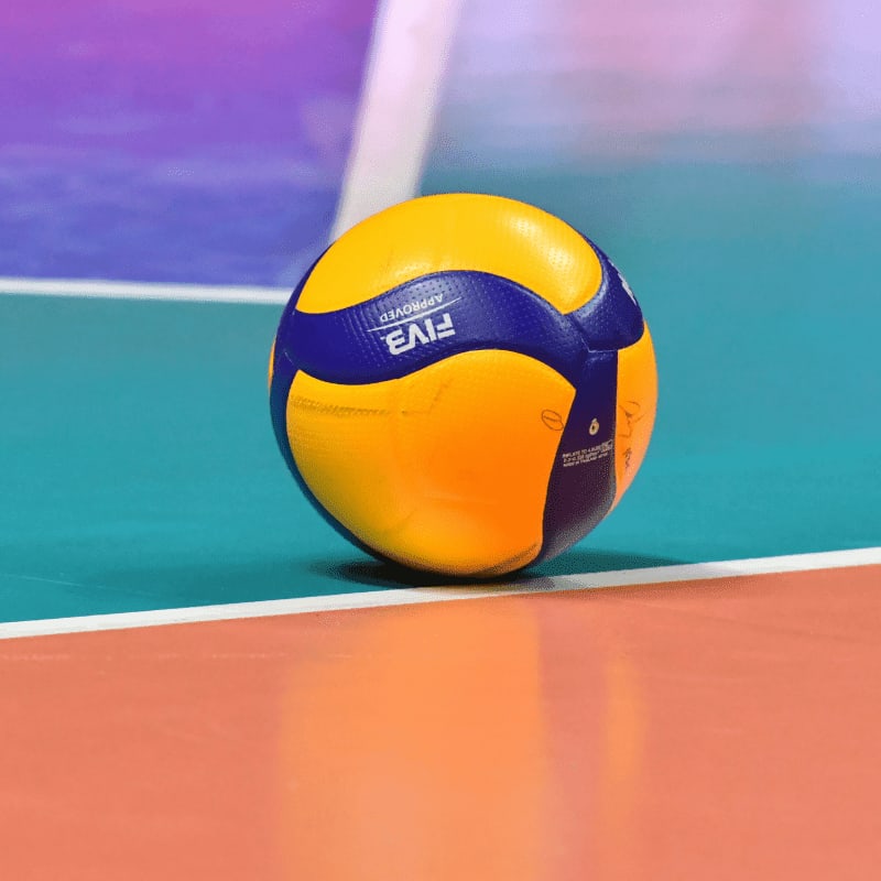 A yellow and blue volleyball on a colorful indoor court floor
