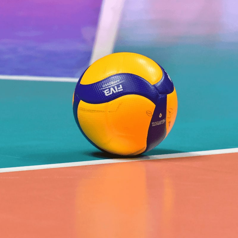 A yellow and blue volleyball on a colorful indoor court floor