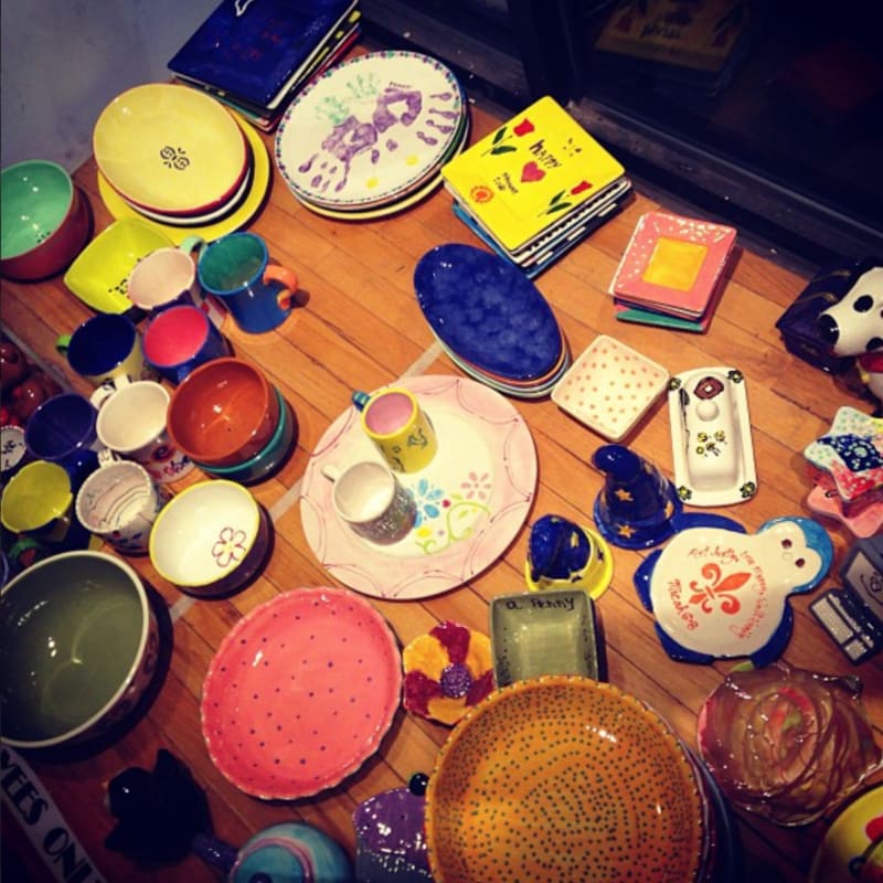 Colorful ceramic dishes and mugs are scattered across a wooden surface, with a dark, out-of-focus background.