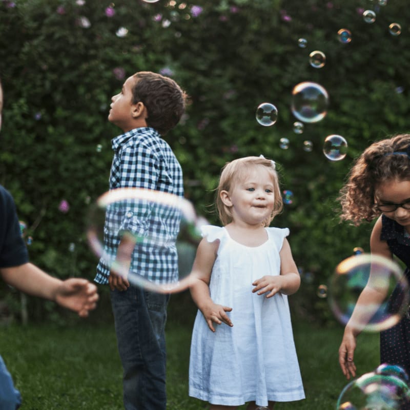 Four children playing with floating bubbles in a green garden