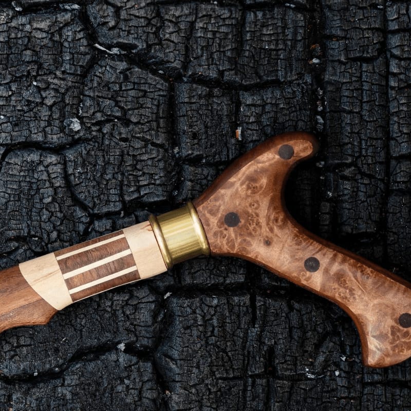 A carved wooden handle with brass accents rests on a charred, cracked surface.