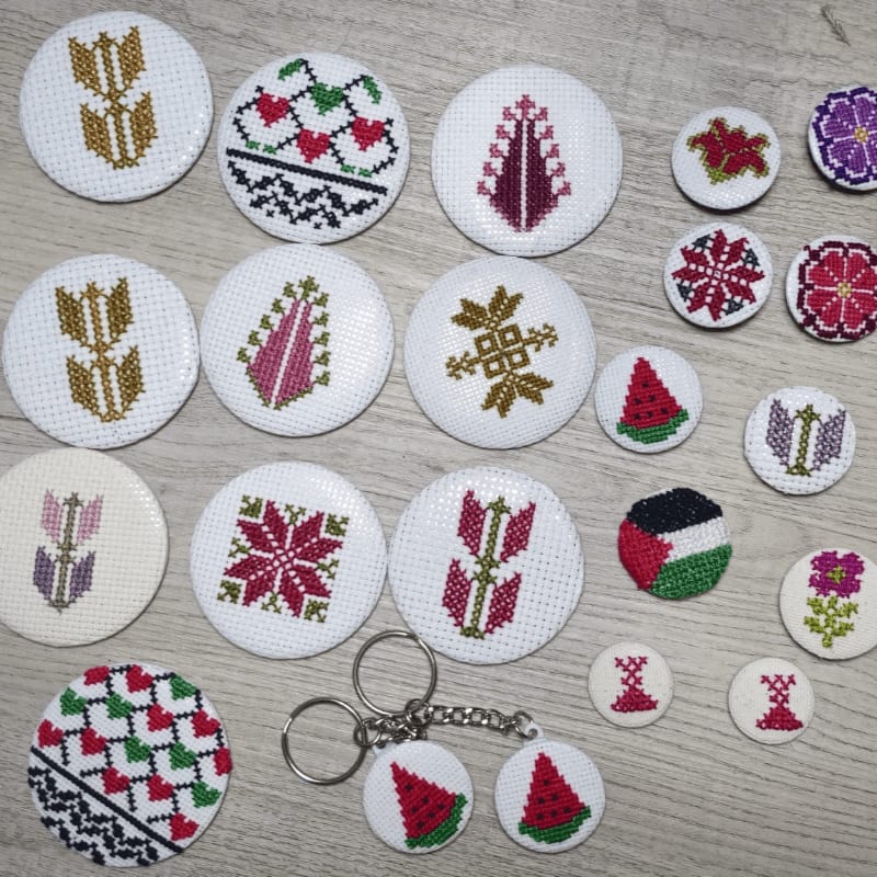 A collection of circular cross-stitch creations, featuring floral and geometric patterns, as well as watermelon slices and a Palestinian flag, are arranged on a wooden surface.