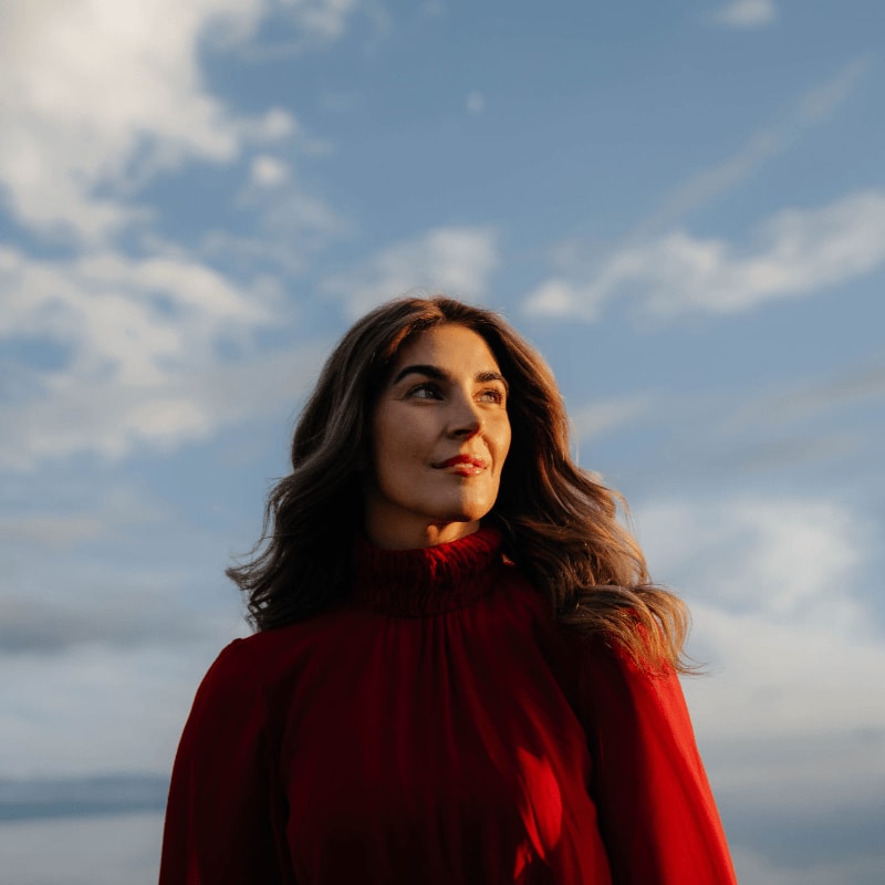 A woman in a red dress looks up at a cloudy blue sky.