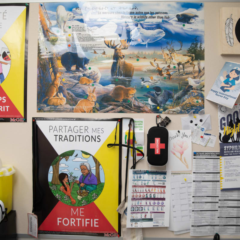A colorful poster of Indigenous traditions and wildlife hangs on a bulletin board with various other notices and a first-aid kit in the foreground.