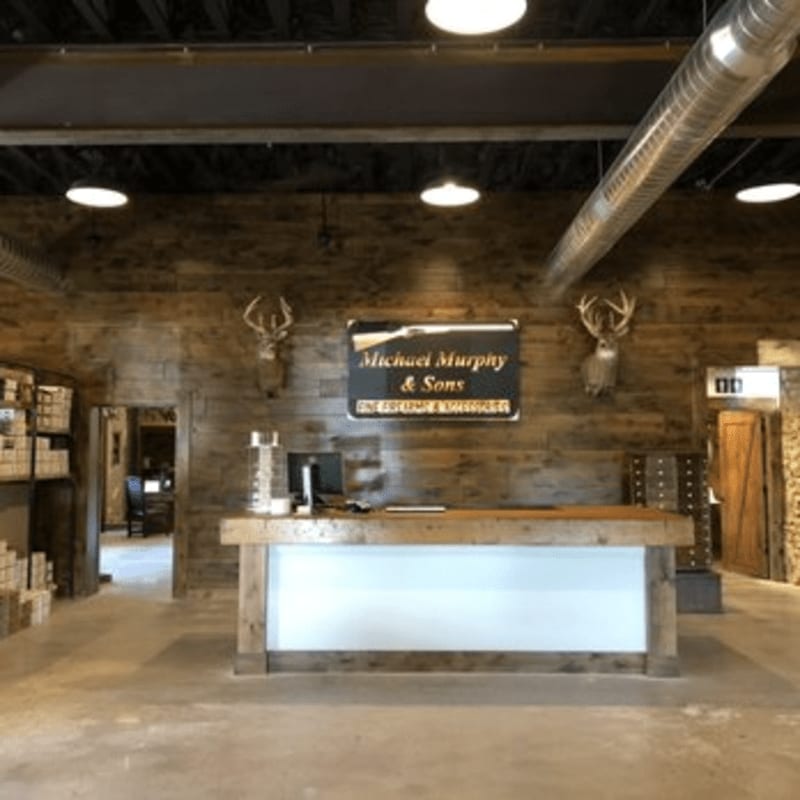 A rustic reception desk with a computer sits in the foreground, while a wooden wall with mounted deer antlers and a business sign adorns the background.