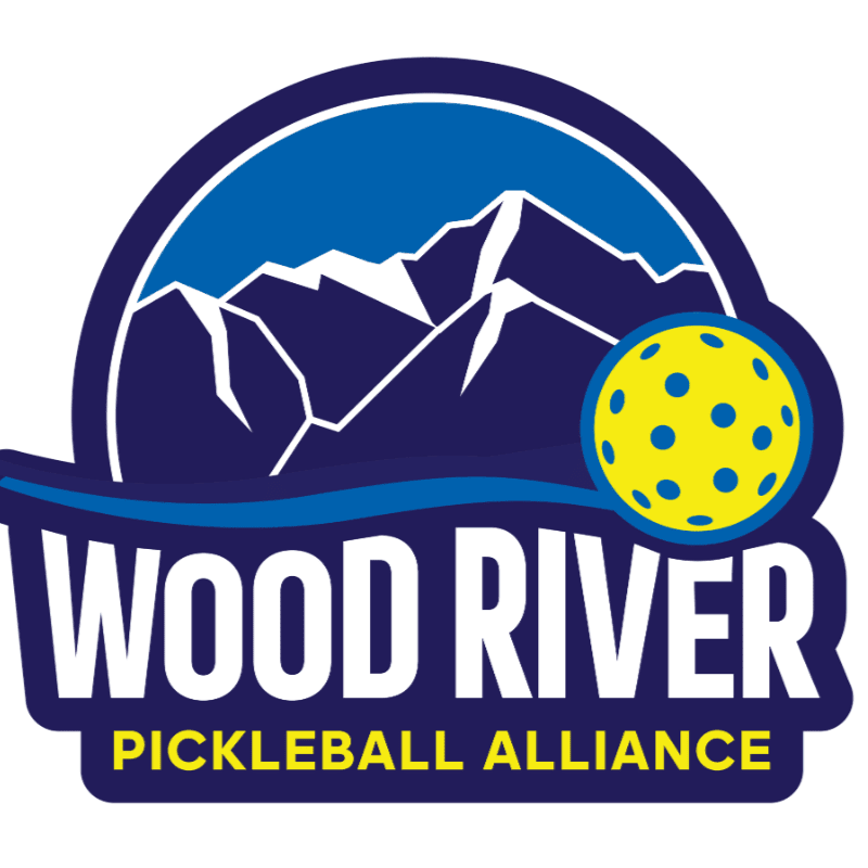 A yellow pickleball sits in front of a dark blue mountain range under a bright blue sky, with "WOOD RIVER PICKLEBALL ALLIANCE" written in white and yellow text below.