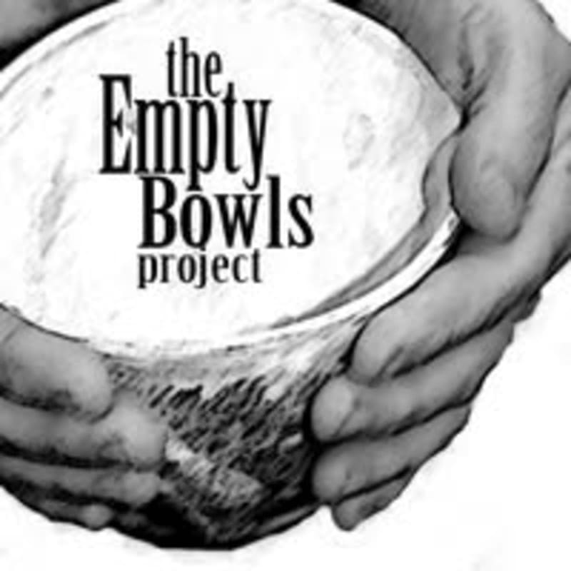 Hands cradle an empty bowl with the words "the Empty Bowls project" printed on it against a textured, light background.