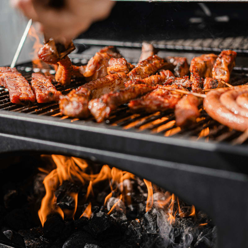 a person grilling hot dogs and sausages on a grill