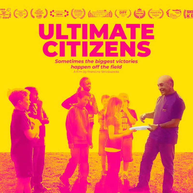 A group of children and an adult stand on a grassy field, with the title "ULTIMATE CITIZENS" prominently displayed in the background.