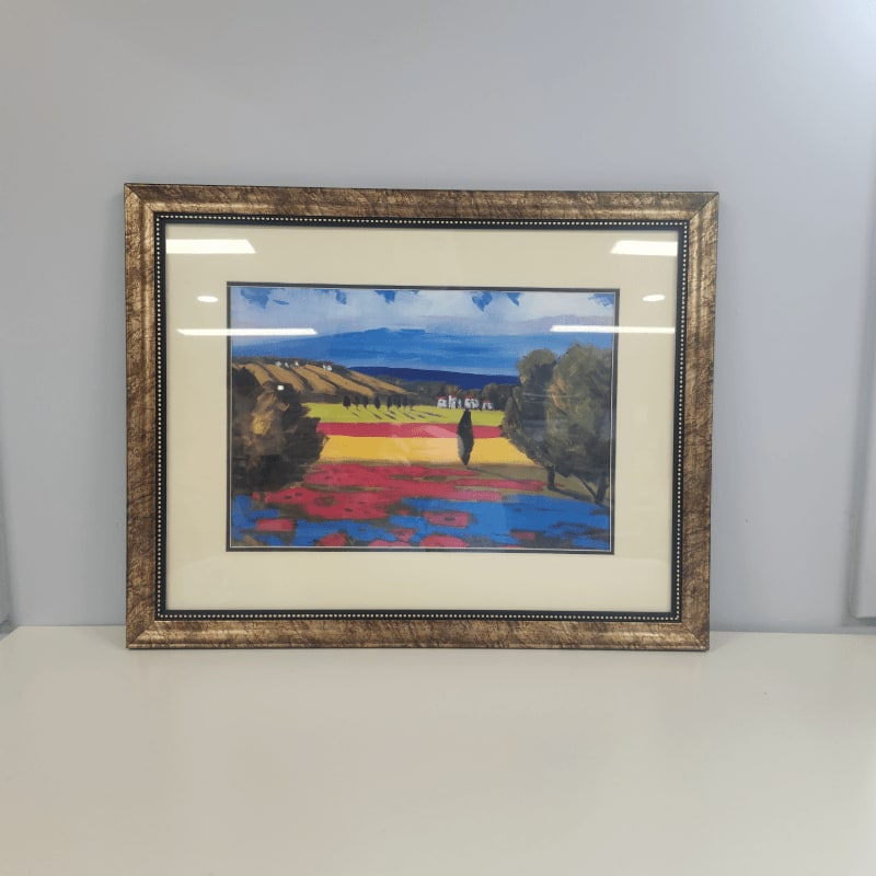 A framed painting displays a vibrant, abstract landscape with a solitary tree in the foreground and rolling hills under a blue sky in the background.
