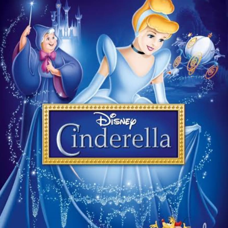 Cinderella in her blue gown is in the foreground, with the Fairy Godmother and a carriage in the background, all under a castle.