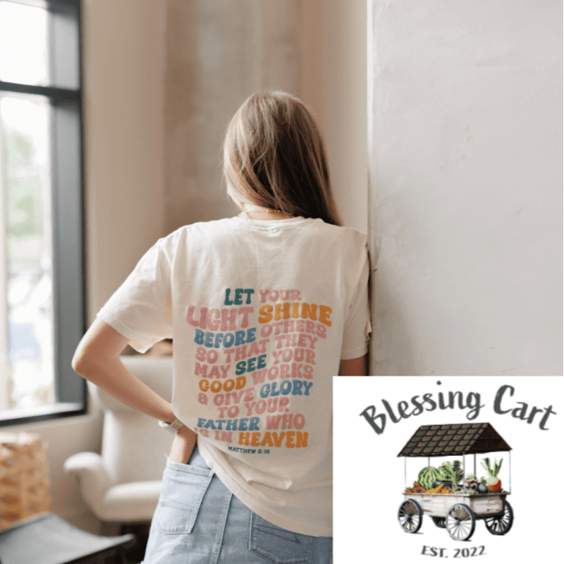A woman in a cream t-shirt with a Bible verse printed on the back stands in a brightly lit room with a logo in the corner.