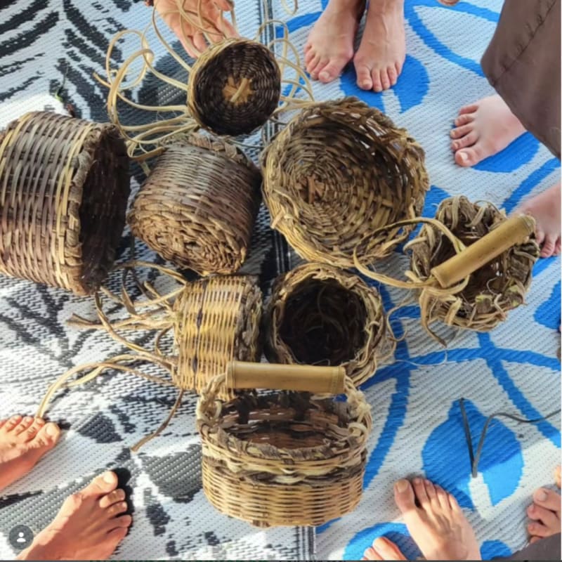Several woven baskets are arranged on a patterned mat, surrounded by bare feet.