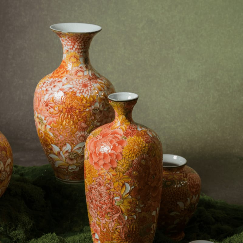Three ornate orange and yellow floral vases stand on a mossy surface against a softly lit, muted green background.