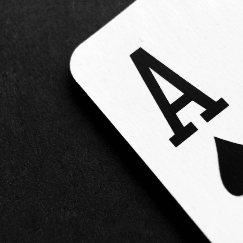 A close-up of an ace of spades card rests on a dark, textured surface.