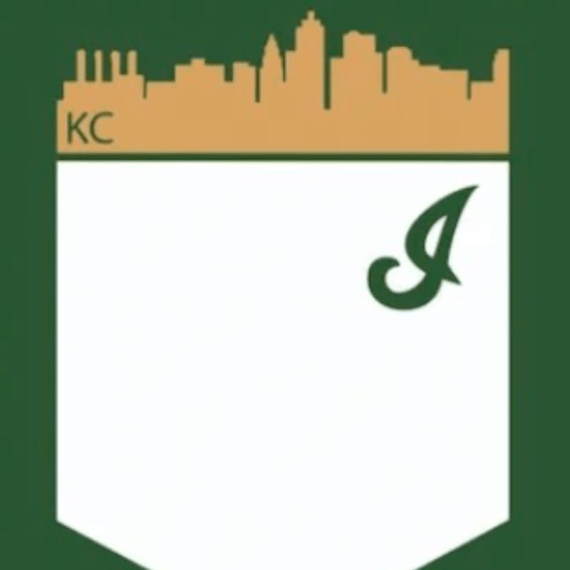 A white shield with a green "I" in the foreground is set against a green background, topped by a tan skyline silhouette with "KC" to the left.