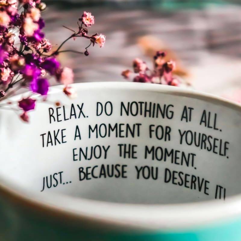 A ceramic mug with printed text and purple flowers in a soft focus
