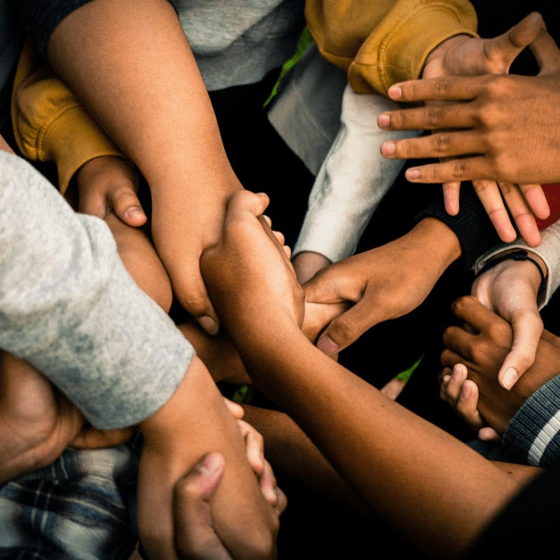 A diverse group of hands clasped together in unity, with blurred clothing in the background.