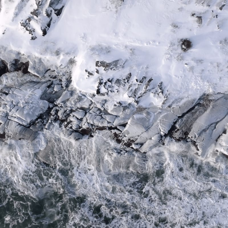 Crashing waves churn against a snow-dusted rocky shoreline.