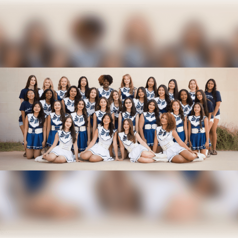 A group of young women in matching blue and white uniforms pose for a photo, with a blurred background of a building and some greenery.