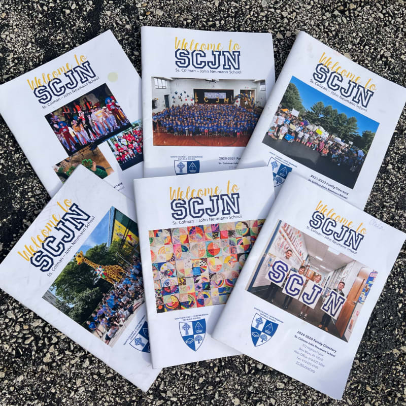Several brochures with "Welcome to SCJN" on the cover are scattered on a dark, textured surface, with each brochure displaying different photos of students and school events.