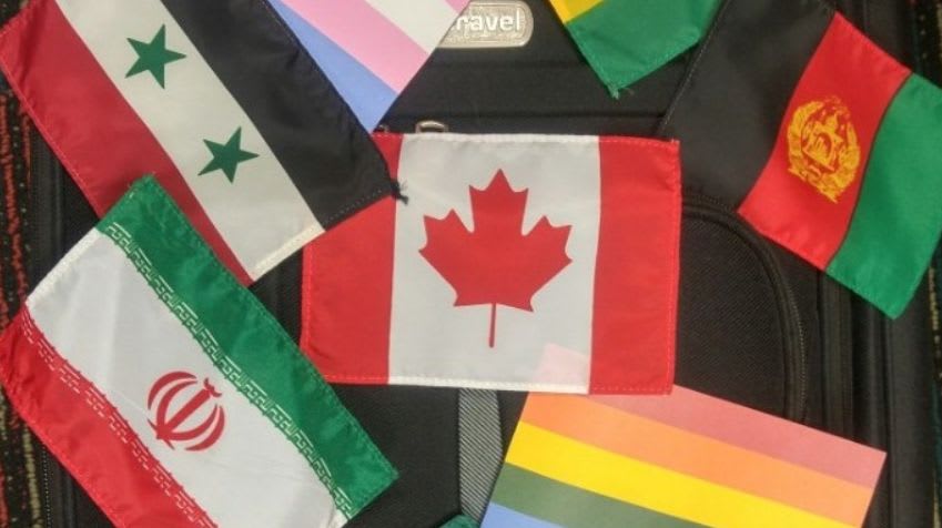 Several national and pride flags are arranged on a dark, textured surface, with the Canadian flag prominently displayed in the center.