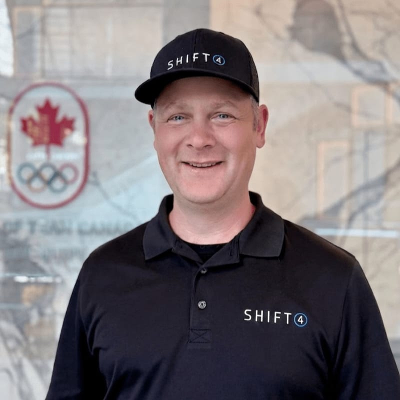 A smiling man in a black "SHIFT4" hat and polo shirt stands in front of a blurred background featuring the Canadian Olympic logo.