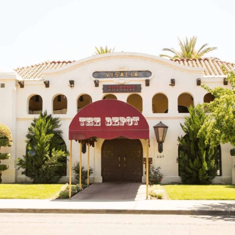 A red awning with "THE DEPOT" written on it covers the entrance to a white building with arched windows, set against a clear sky with palm trees visible in the background.