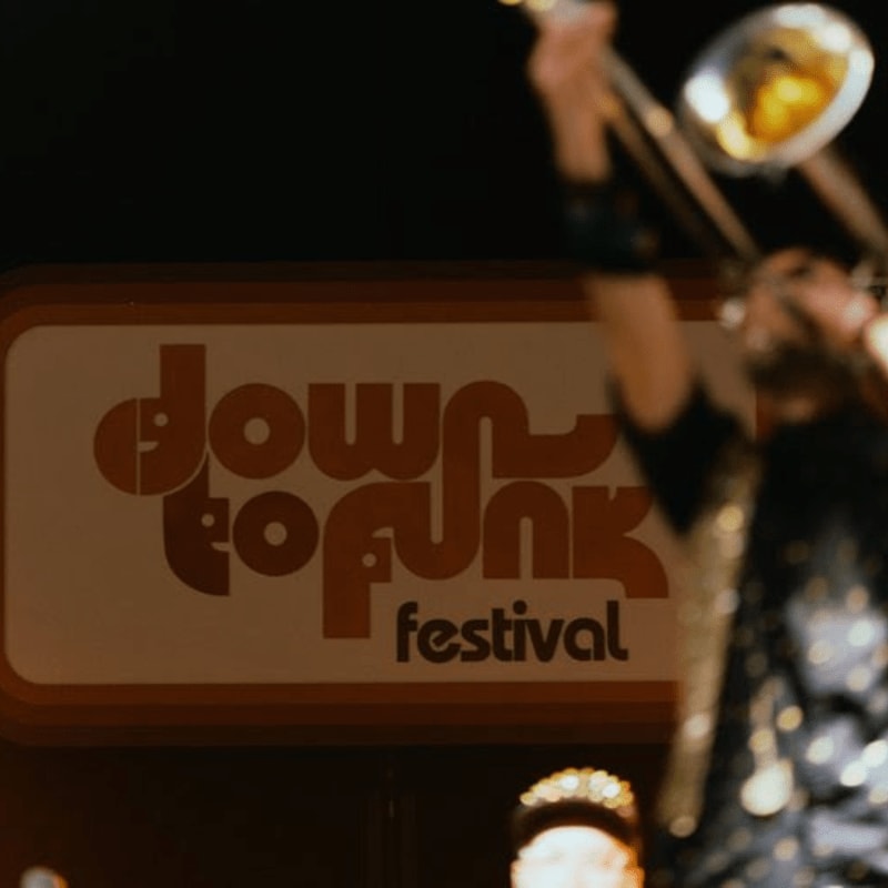 A trombonist plays in front of a "down to funk festival" sign.