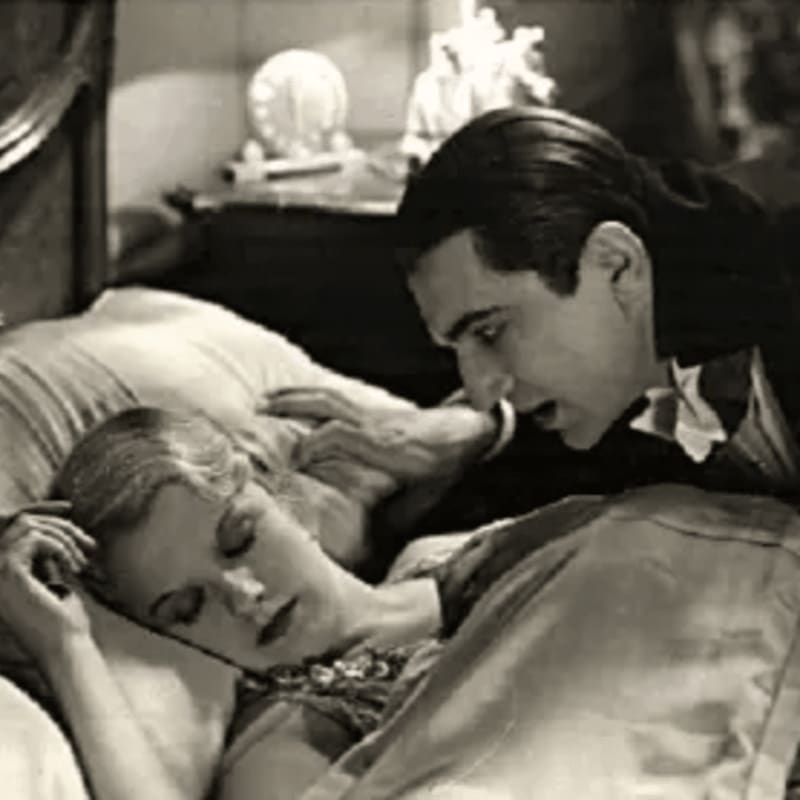 A man with dark hair and a cape leans over a sleeping woman in a bed, with a lamp and ornate headboard visible in the background.