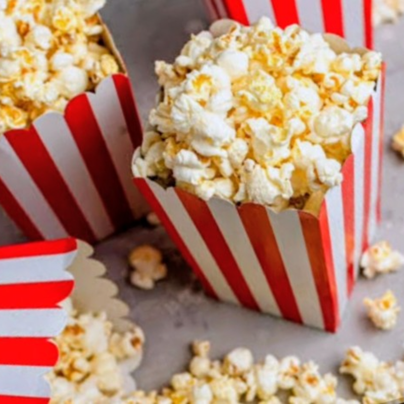 Several red and white striped boxes overflow with popcorn in the foreground, with scattered kernels on a gray surface in the background.
