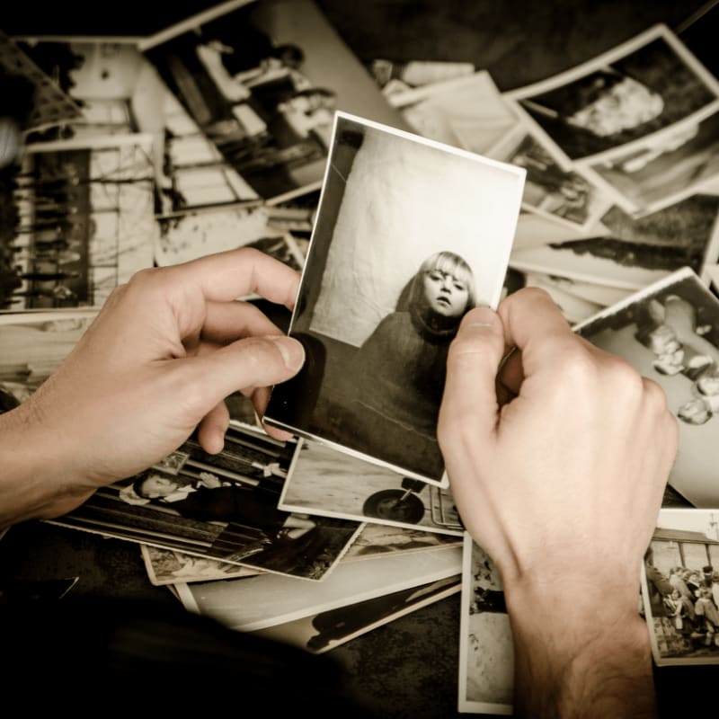 Hands hold a sepia-toned photograph of a child in front of a pile of similar vintage photos.