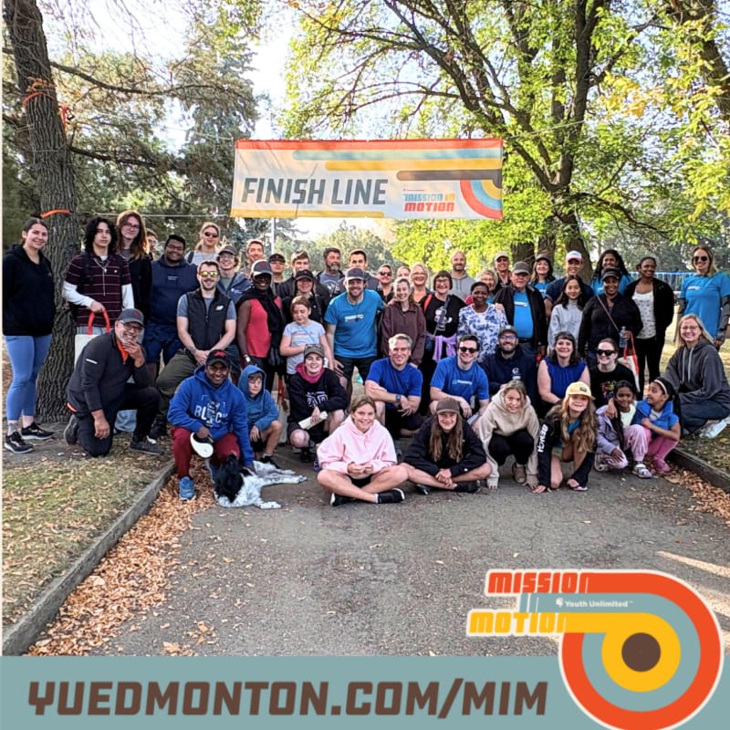 A group of people pose for a photo in front of a "Finish Line" banner, with trees and a park setting in the background.