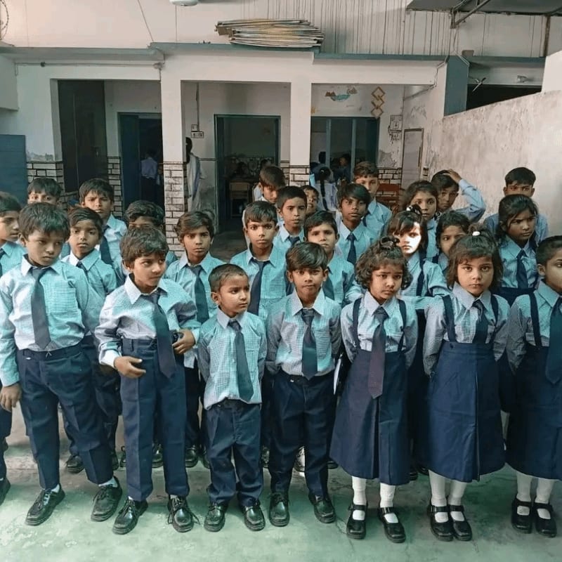A group of young students in uniform stand in a courtyard with a building in the background.