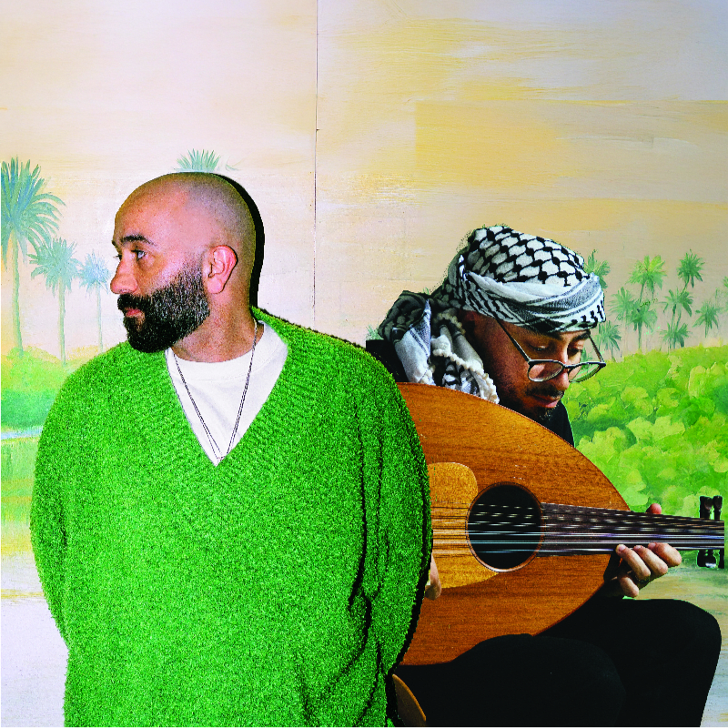 A bald man in a green sweater stands in the foreground, while a man wearing a keffiyeh plays an oud in the background against a painted landscape of palm trees and water.