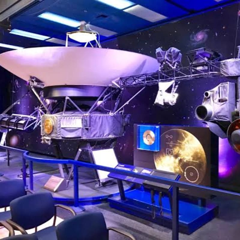 A large spacecraft model with a dish antenna is displayed in the foreground, set against a backdrop of a starry galaxy.