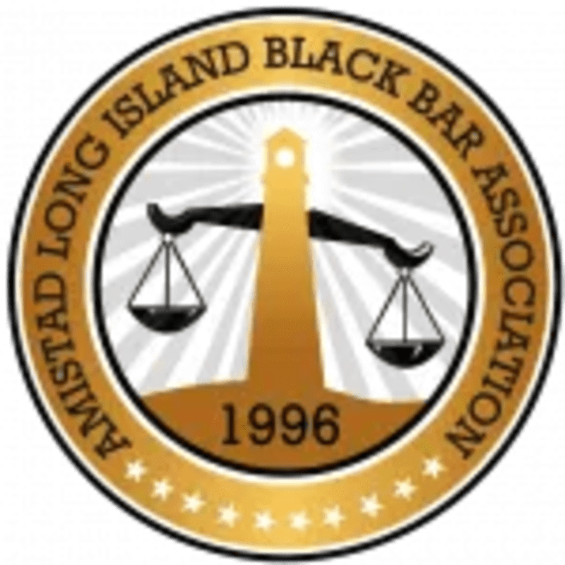 A golden lighthouse with scales of justice in the foreground is set against a background of radiating white lines within a circular emblem that reads "Amistad Long Island Black Bar Association 1996".