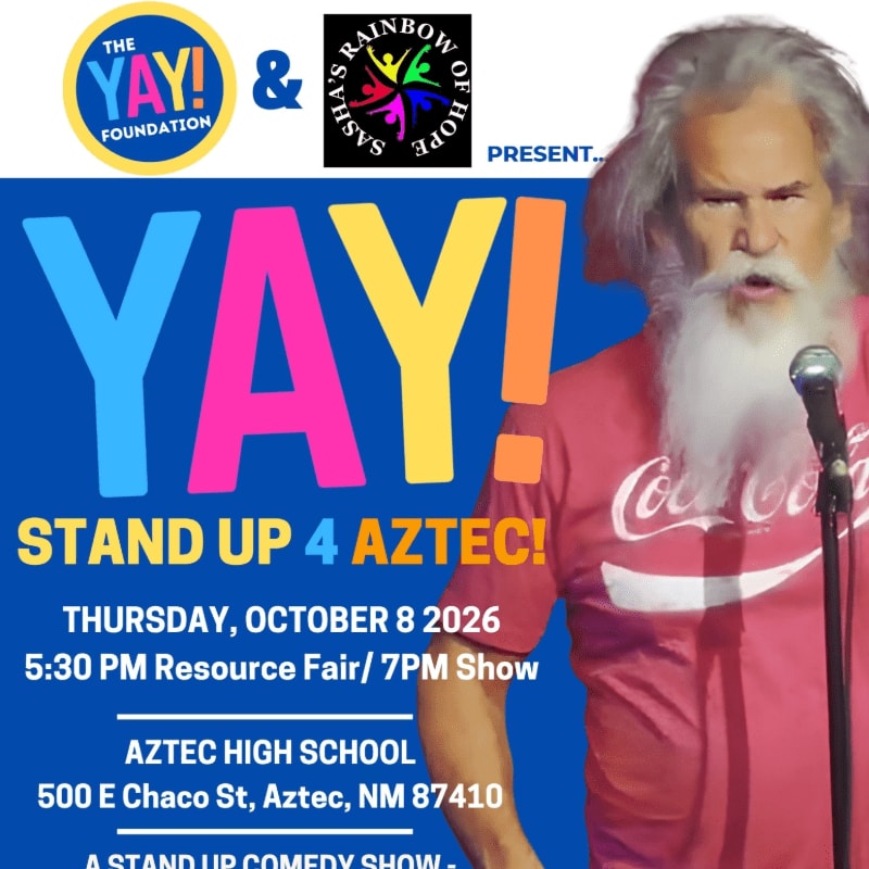 A man with a long white beard and a pink Coca-Cola shirt stands in front of a colorful "YAY! STAND UP 4 AZTEC!" poster, with logos for The Yay! Foundation and Sasha's Rainbow of Hope in the background.
