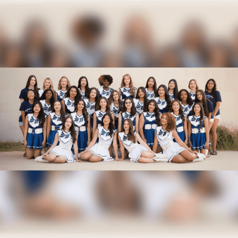 A group of young women in matching blue and white uniforms pose for a photo, with a blurred background of a building and some greenery.