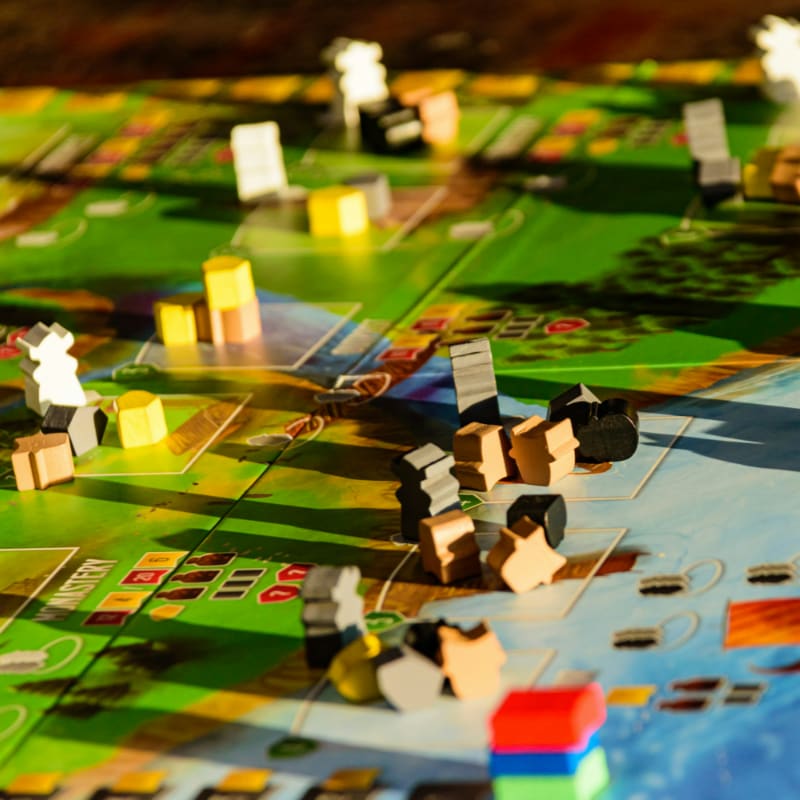 Colorful wooden game pieces are scattered across a vibrant board game with a blurred background.